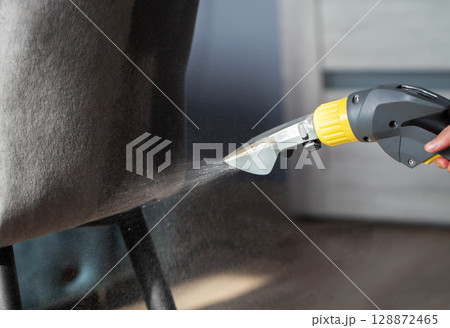 Spraying a chemical from a washing vacuum cleaner when cleaning the fabric upholstery of a chair. Cleaning services, industry Spraying a chemical from a washing vacuum cleaner when cleaning the fabric upholstery of a chair. Cleaning services, industry 128872465