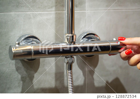 Women's fingers with red manicure regulate the water temperature in the shower tap, close-up Women's fingers with red manicure regulate the water temperature in the shower tap, close-up 128872534