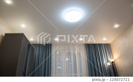 Gray sliding wardrobe in a studio apartment against the background of turquoise curtains and a suspended ceiling with diode lighting. Copy space for text 128872721