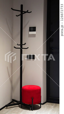 Modern red pouf in hallway corner for sitting against clothes rack background, interior 128872733