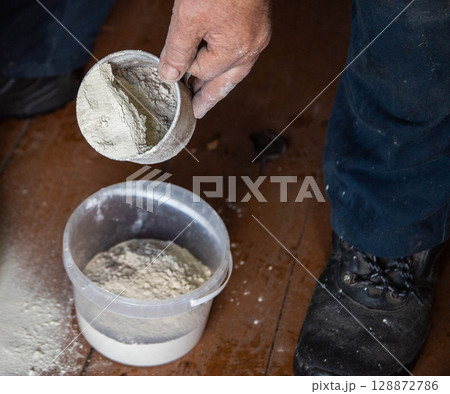 Dolomite flour in a mug against the background of a bucket, fertilizing the soil at the dacha, close-up 128872786