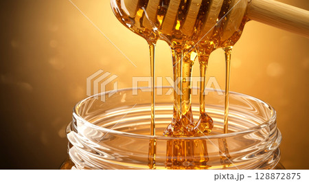 Golden honey dripping from a dipper into a jar. 128872875