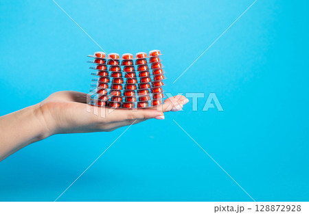 Stack of red pills on palm in hand on blue background. Concept of fluoroquinolone antibiotic pills in treatment of diseases. Copy space for text, closeup 128872928