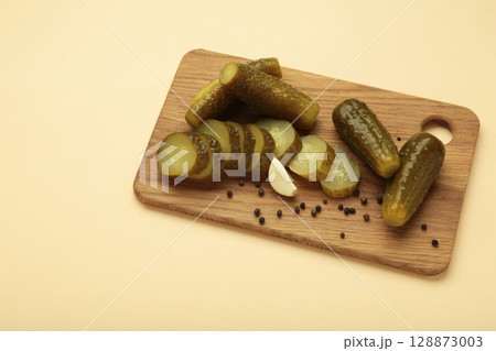 Marinated pickled cucumber on cutting board on beige background. Marinated pickled cucumber on cutting board on beige background. 128873003