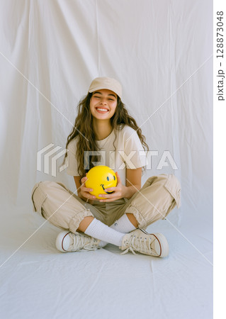 A woman is sitting on the floor with a yellow smiley face ball in her hand A woman is sitting on the floor with a yellow smiley face ball in her hand 128873048