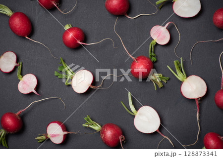 Scattered Fresh Radishes And Slices Artistically Arranged On Dark Surface 128873341