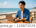 海の見えるカフェでリモートワークする若い男性・ワーケーションイメージ 128873528