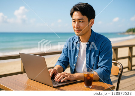 海の見えるカフェでリモートワークする若い男性・ワーケーションイメージ 128873528