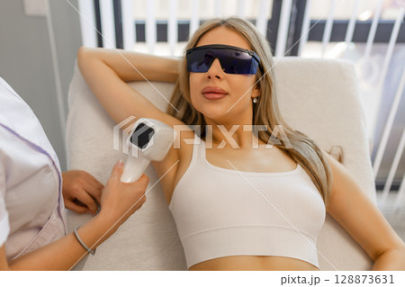 Hair removal procedure. Cropped shot of young fit woman client receiving laser hair removal procedure on body in beauty clinic. Women beauty and cosmetology concept Hair removal procedure. Cropped shot of young fit woman client receiving laser hair removal procedure on body in beauty clinic. Women beauty and cosmetology concept 128873631