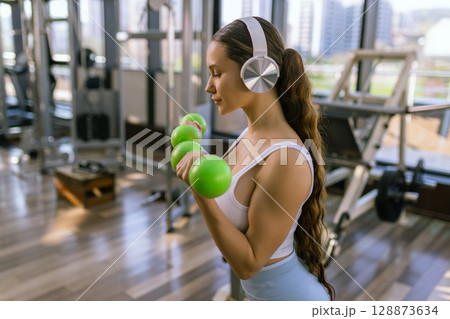 Attractive young woman working out with dumbbells at a gym. Attractive young woman working out with dumbbells at a gym. 128873634