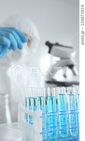 Scientific researcher wearing protective equipment, carefully pipetting liquid into test tubes while conducting medical research experiment. Medicine, healthcare and science concept 128873819