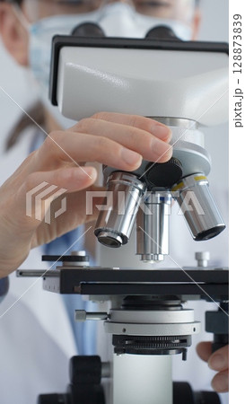 Female scientist wearing lab coat and protective glasses using a modern microscope in a laboratory setting, conducting research and experiments, close up. Health care, medicine and science concept Female scientist wearing lab coat and protective glasses using a modern microscope in a laboratory setting, conducting research and experiments, close up. Health care, medicine and science concept 128873839