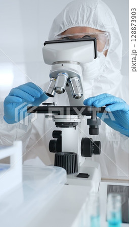 Scientific researcher wearing protective gear adjusting microscope, analyzing lab samples with precision in sterile research environment. Medicine, healthcare and science concept Scientific researcher wearing protective gear adjusting microscope, analyzing lab samples with precision in sterile research environment. Medicine, healthcare and science concept 128873903