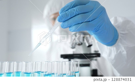 Scientific researcher wearing protective equipment, carefully pipetting liquid into test tubes while conducting medical research experiment. Medicine, healthcare and science concept Scientific researcher wearing protective equipment, carefully pipetting liquid into test tubes while conducting medical research experiment. Medicine, healthcare and science concept 128874031