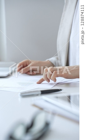Businesswoman reviewing financial documents and charts, performing data analysis for business planning and decision making in a professional office background. Business people concept 128874111