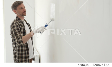 Professional house painter wearing gloves painting a white wall with a paint roller, working on a home renovation project, creating a fresh and clean look Professional house painter wearing gloves painting a white wall with a paint roller, working on a home renovation project, creating a fresh and clean look 128874122