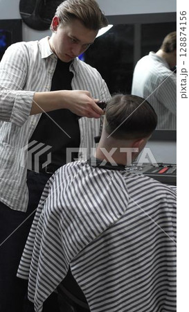 Professional barber carefully trimming customer's hair with electric clipper, providing a stylish and precise haircut in a modern barbershop environment Professional barber carefully trimming customer's hair with electric clipper, providing a stylish and precise haircut in a modern barbershop environment 128874156