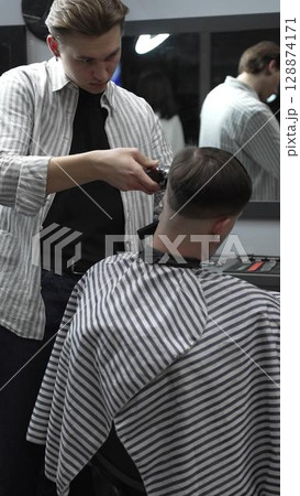 Professional barber carefully trimming customer's hair with electric clipper, providing a stylish and precise haircut in a modern barbershop environment Professional barber carefully trimming customer's hair with electric clipper, providing a stylish and precise haircut in a modern barbershop environment 128874171