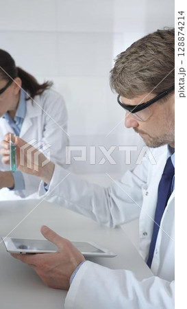 Medical researchers, male and female, examining laboratory samples under microscope and digital tablet during joint scientific research. Medicine and science, teamwork concept 128874214