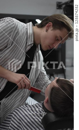 Professional barber trimming customer's hair with electric clipper, focusing on precise nape grooming within contemporary barbershop interior design 128874282