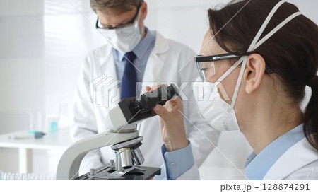 Two scientists, a man and a woman, in lab coats and protective gear, conduct research in a sterile laboratory. Concept of medicine and science 128874291