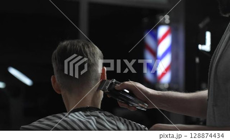 Skilled barber trimming client's hair with electric razor, creating precise contemporary hairstyle inside sleek urban barbershop setting Skilled barber trimming client's hair with electric razor, creating precise contemporary hairstyle inside sleek urban barbershop setting 128874434