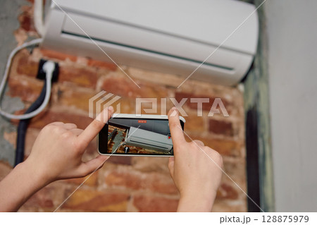 Person taking photo of air conditioner on wall with smartphone 128875979