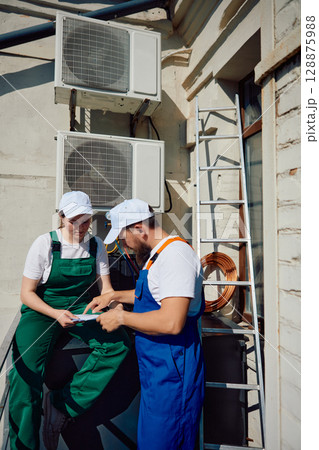 Technicians inspecting air conditioning unit on rooftop of building 128875988