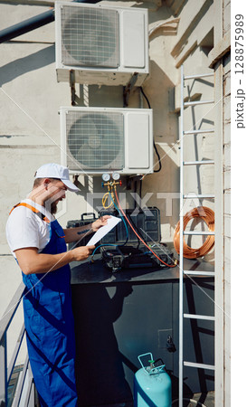 Technician inspecting rooftop air conditioning system with tools and equipment Technician inspecting rooftop air conditioning system with tools and equipment 128875989