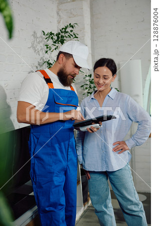 Technician smiling while demonstrating repair details to homeowner on tablet inside Technician smiling while demonstrating repair details to homeowner on tablet inside 128876004