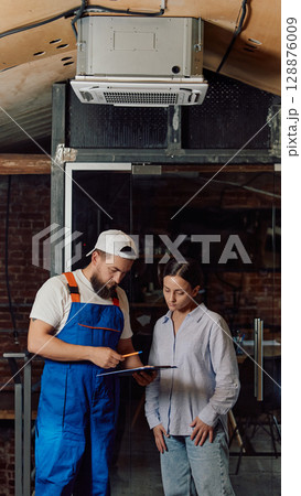 Technician explaining air conditioning system to customer in industrial space 128876009