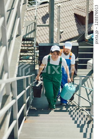 Employees walking up external steps with tools and equipment for building upkeep 128876013