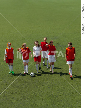 Young women football players on grass field holding soccer ball 128876027