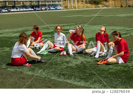Women football team resting on field during sunny training session Women football team resting on field during sunny training session 128876039