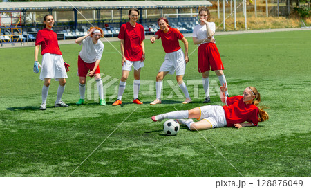 Smiling female footballers standing and joking around fallen teammate Smiling female footballers standing and joking around fallen teammate 128876049