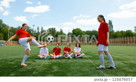 Female football players practicing on green field under clear sky 128876057