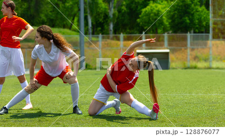Female football athletes stretching on a sunny day on a grassy field 128876077