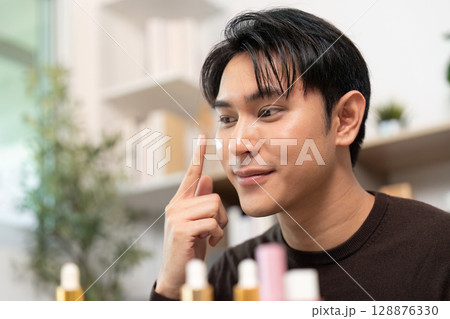 Skincare Application. Young man applying serum with focus and joy. Skincare Application. Young man applying serum with focus and joy. 128876330