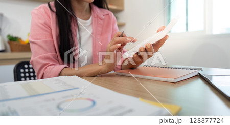 Work from Home Individual using smartphone while analyzing data reports Work from Home Individual using smartphone while analyzing data reports 128877724
