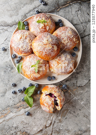 Close-up of brioche buns with blueberries, almond flakes and powdered sugar in a plate. Vertical top view 128877940
