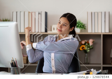 Office Syndrome: Young woman performing arm stretches at her workstation Office Syndrome: Young woman performing arm stretches at her workstation 128878544