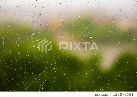 Raindrops on window glass creating a blurred view of vibrant greenery outside 128878581