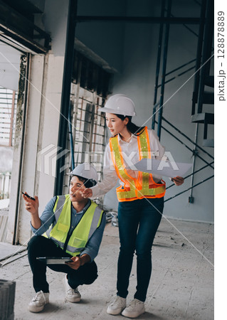 Construction manager and engineer dressed in orange work vests and hard helmets explore construction documentation on the building site near the steel frames 128878889