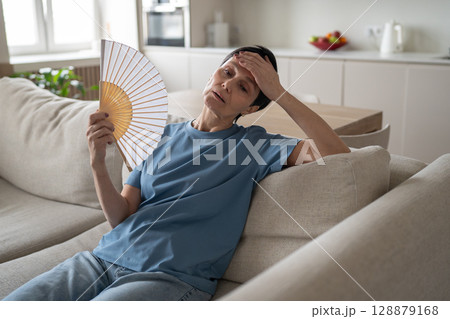 Tired stressed woman fanning home sweating hard no conditioning suffocating difficulty breathe Tired stressed woman fanning home sweating hard no conditioning suffocating difficulty breathe 128879168