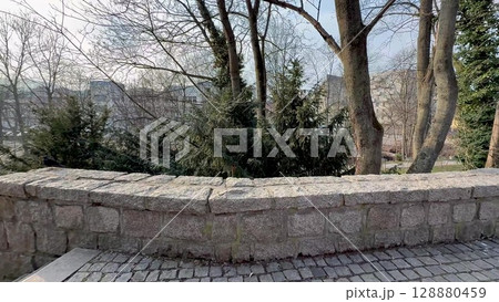 A beautiful and serene park scene featuring a charming stone wall along with lush trees 128880459