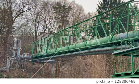 An Industrial Bridge with a Green Pipeline Flowing Through Lush Trees Nearby the Structure An Industrial Bridge with a Green Pipeline Flowing Through Lush Trees Nearby the Structure 128880469
