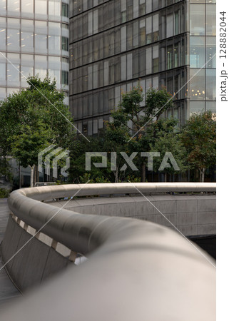The sleek stainless steel handrail, Leading the eye towards the background where modern glass buildings with glimpses of green trees. The sleek stainless steel handrail, Leading the eye towards the background where modern glass buildings with glimpses of green trees. 128882044