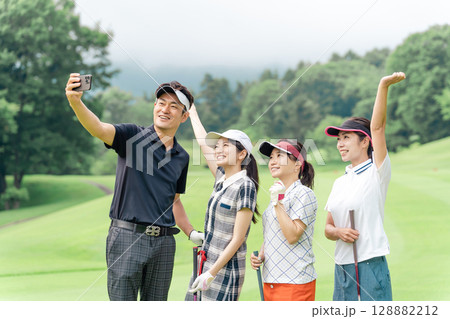 ゴルフ場でスマホを使って自撮り・セルフィー・記念写真を撮るゴルファーの男女 128882212