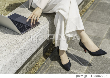 ベンチに座ってノートパソコンを操作する若いビジネスウーマンの足元のアップ 128882292