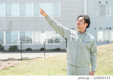 会社の前で空を指差す作業着姿の中年ビジネスマン男性 会社の前で空を指差す作業着姿の中年ビジネスマン男性 128883153